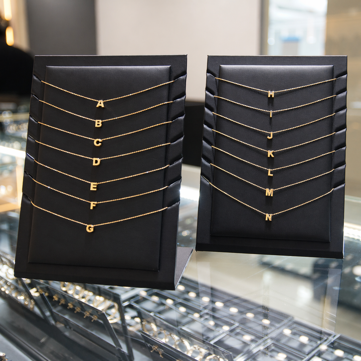 Two black display stands with gold necklaces labeled A to N on a reflective surface.