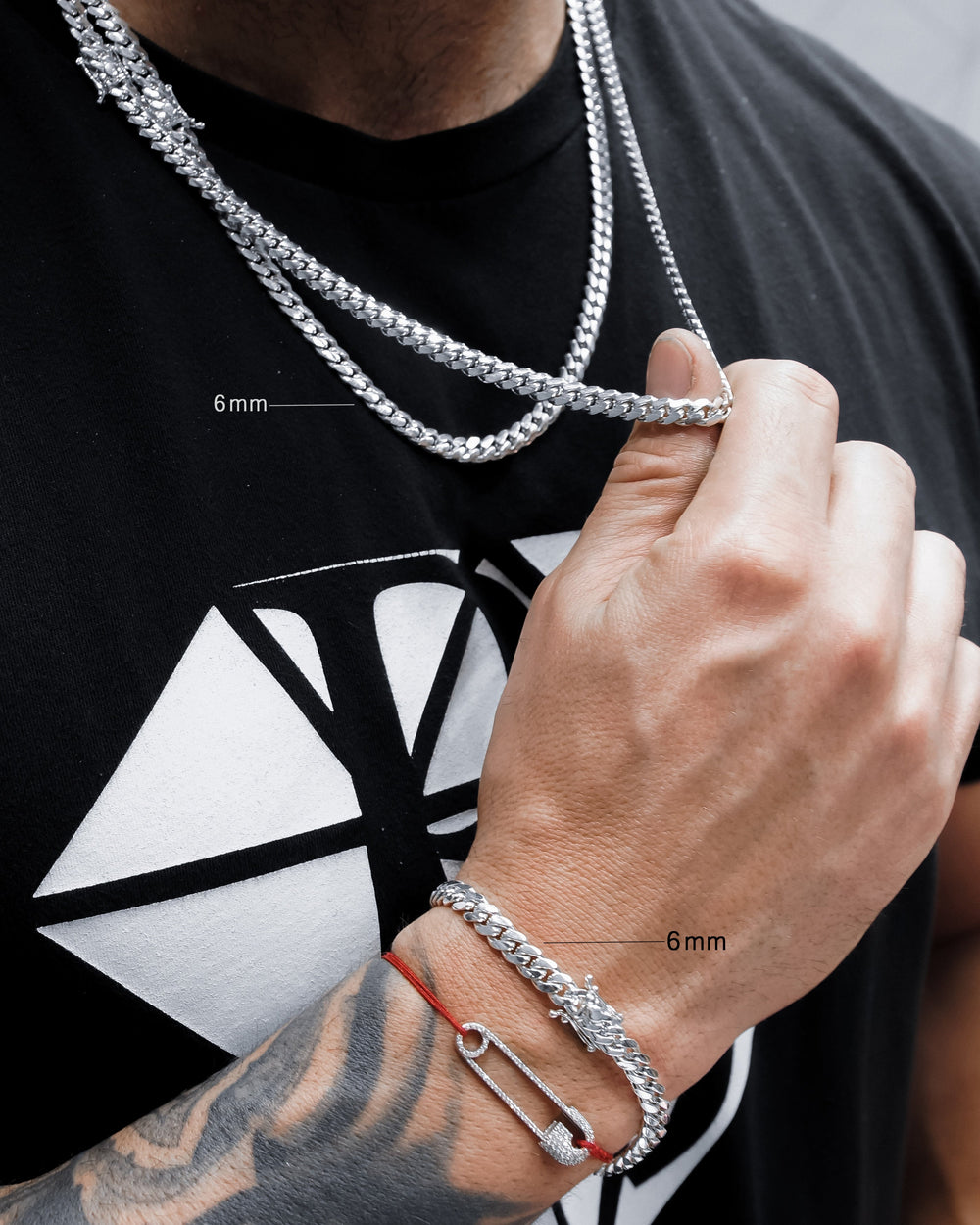 Person wearing a silver chain necklace and bracelet with close-up measurements on a black t-shirt with a white design.